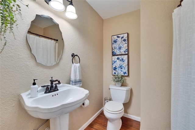 full bath featuring a textured wall, toilet, a sink, wood finished floors, and baseboards