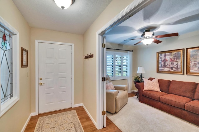 foyer entrance featuring a textured ceiling, light wood finished floors, a ceiling fan, and baseboards