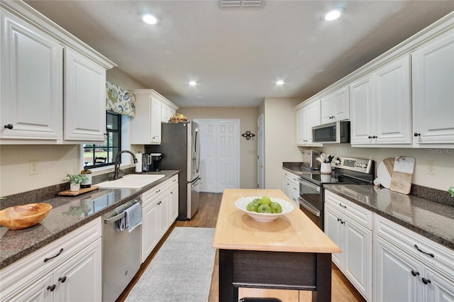 kitchen with white cabinets, dark stone counters, stainless steel appliances, and a sink