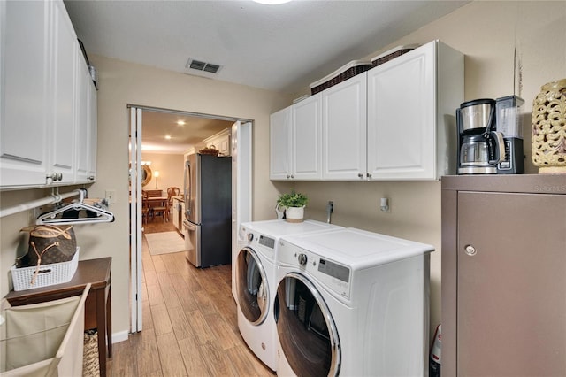 laundry area featuring light wood-style flooring, separate washer and dryer, a sink, visible vents, and cabinet space