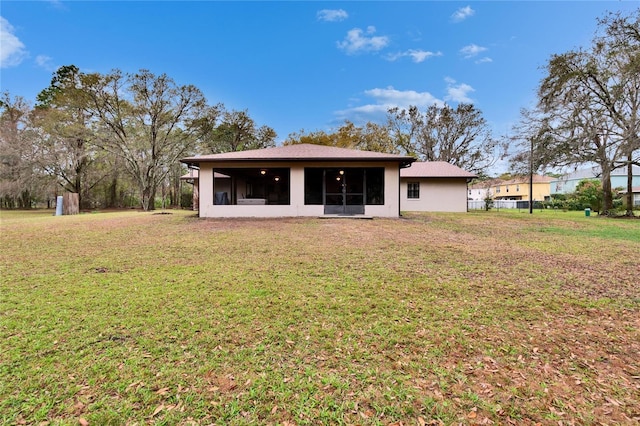 rear view of property featuring a sunroom, a lawn, and stucco siding