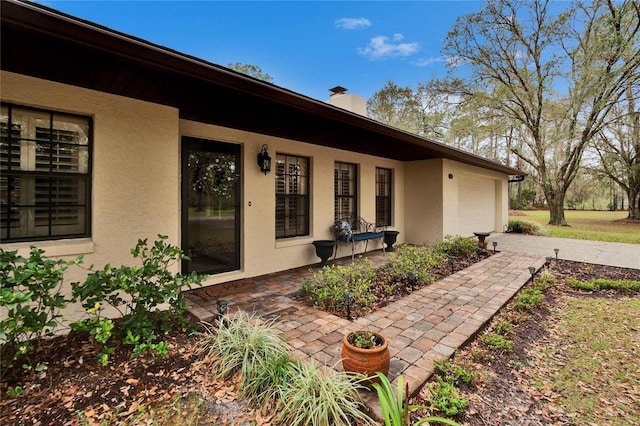 property entrance with a garage, a chimney, and stucco siding