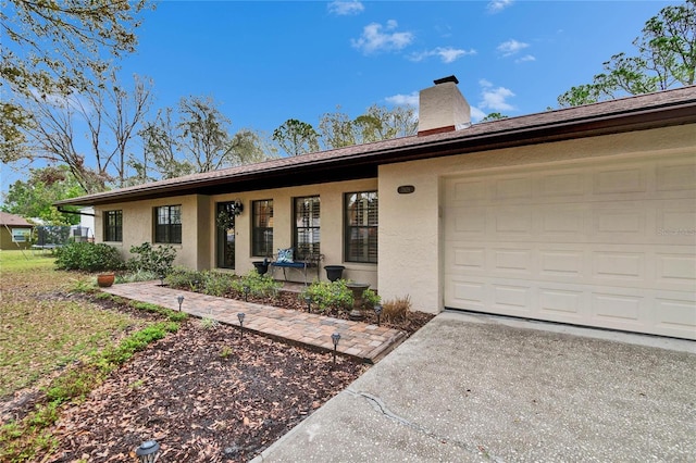 ranch-style house featuring a chimney, stucco siding, covered porch, concrete driveway, and a garage