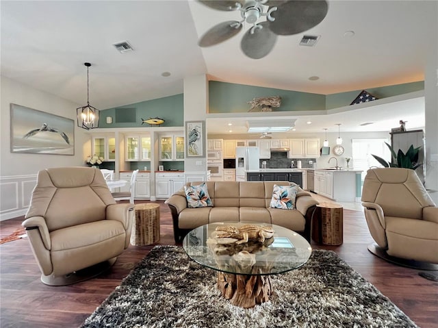 living room featuring ceiling fan with notable chandelier, high vaulted ceiling, dark wood-type flooring, and visible vents