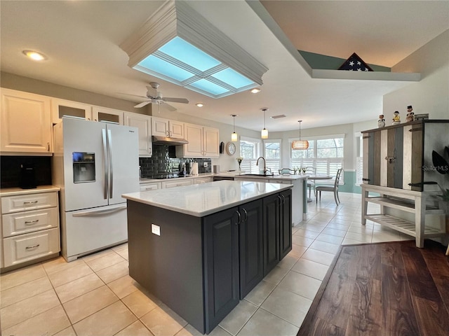 kitchen featuring a skylight, white refrigerator with ice dispenser, decorative backsplash, a kitchen island, and a peninsula