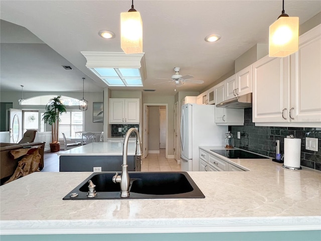 kitchen featuring under cabinet range hood, a sink, black electric cooktop, and decorative backsplash