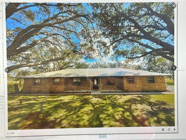 ranch-style house with metal roof, brick siding, and a front yard