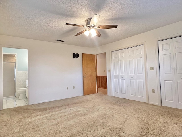 unfurnished bedroom with carpet, two closets, visible vents, a textured ceiling, and ensuite bath