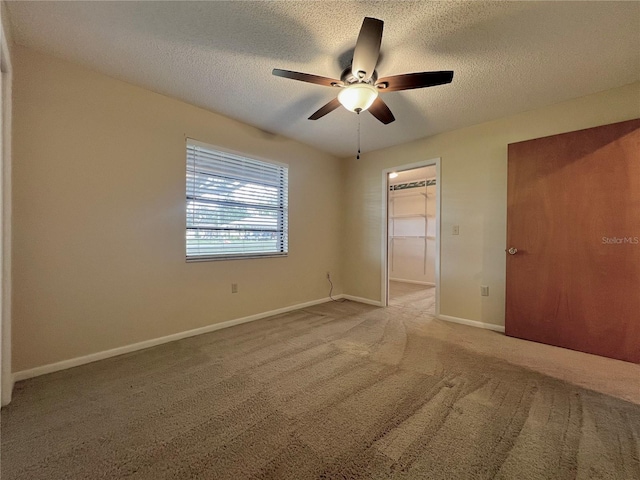 unfurnished bedroom featuring carpet, a walk in closet, a closet, a textured ceiling, and baseboards