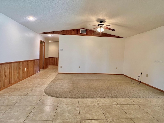 spare room with a textured ceiling, wood walls, visible vents, vaulted ceiling, and wainscoting