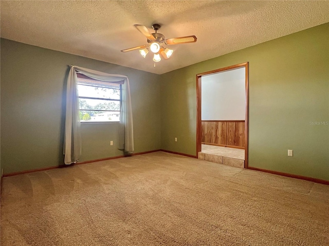 unfurnished room featuring a ceiling fan, wainscoting, light carpet, a textured ceiling, and baseboards