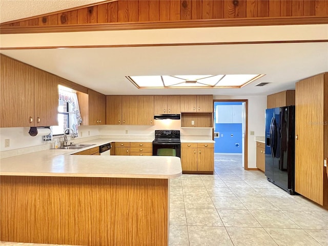 kitchen featuring lofted ceiling with skylight, a peninsula, light countertops, black appliances, and a sink