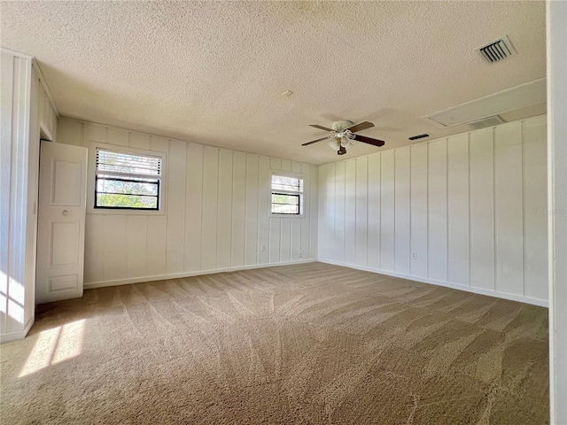 unfurnished room with ceiling fan, a textured ceiling, carpet flooring, visible vents, and attic access