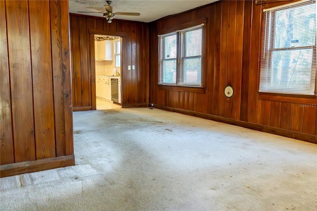 spare room featuring light colored carpet, baseboards, and wood walls