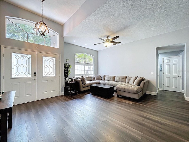 living area featuring ceiling fan with notable chandelier, a textured ceiling, baseboards, and dark wood-style floors