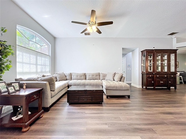 living area with a textured ceiling, wood finished floors, ceiling fan, and visible vents