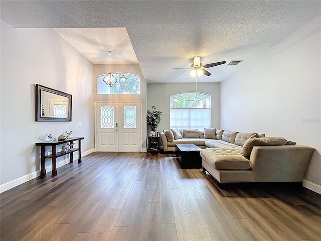 living room with dark wood-style flooring, visible vents, baseboards, and a textured ceiling