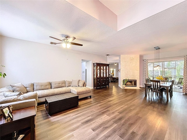 living area featuring visible vents, ceiling fan, a fireplace, a textured ceiling, and wood finished floors