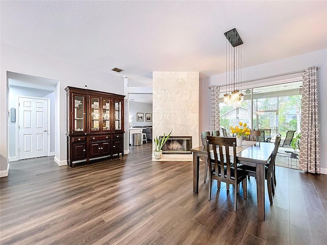 dining room with visible vents, an inviting chandelier, a tiled fireplace, a textured ceiling, and dark wood-type flooring