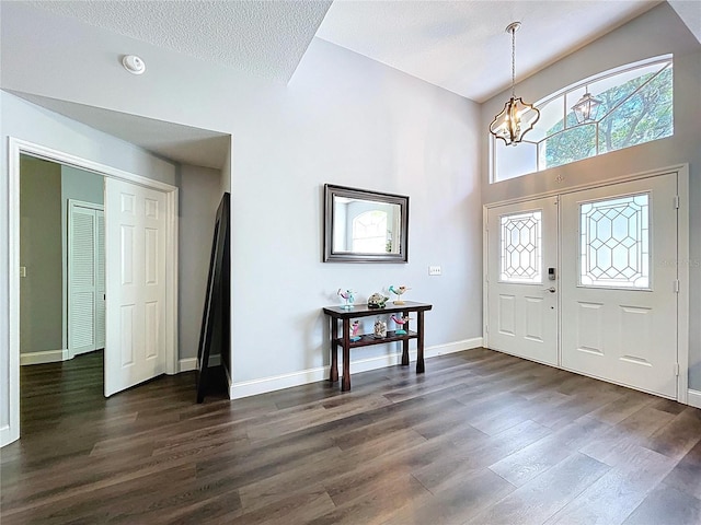 foyer with dark wood-type flooring, baseboards, an inviting chandelier, and a high ceiling