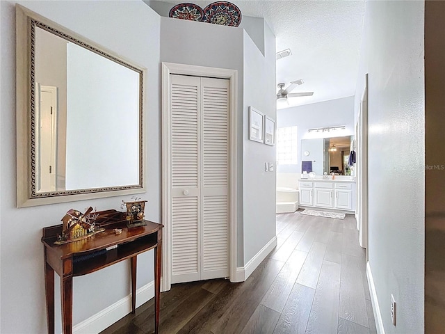 hall featuring visible vents, baseboards, a textured ceiling, and wood finished floors