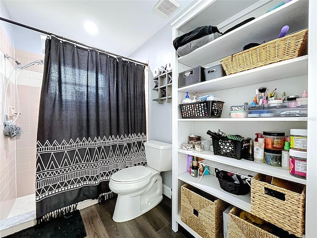full bath with visible vents, toilet, tiled shower, and wood finished floors