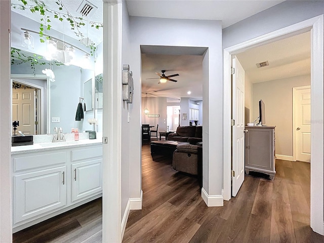 hallway featuring dark wood-type flooring, visible vents, baseboards, and a sink