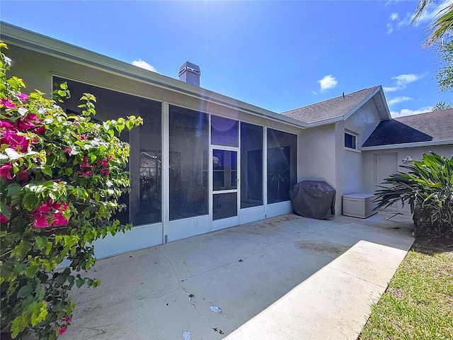 back of property with roof with shingles, a patio, a sunroom, and stucco siding