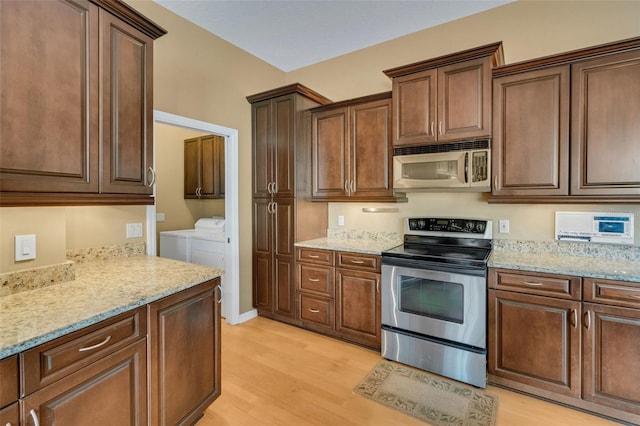 6928 Hayter Ln, Lakeland, FL 33813 - kitchen with washing machine and clothes dryer, light stone counters, dark brown cabinets, light wood-style floors, and stainless steel appliances
