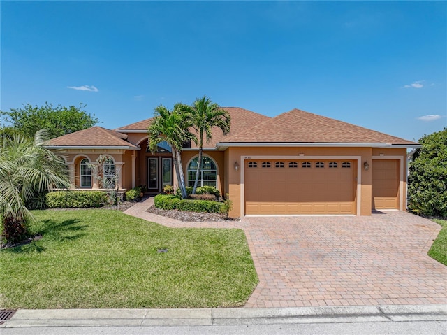 mediterranean / spanish house with stucco siding, an attached garage, decorative driveway, and a front yard