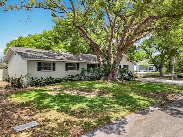 single story home featuring brick siding, a front yard, and roof with shingles