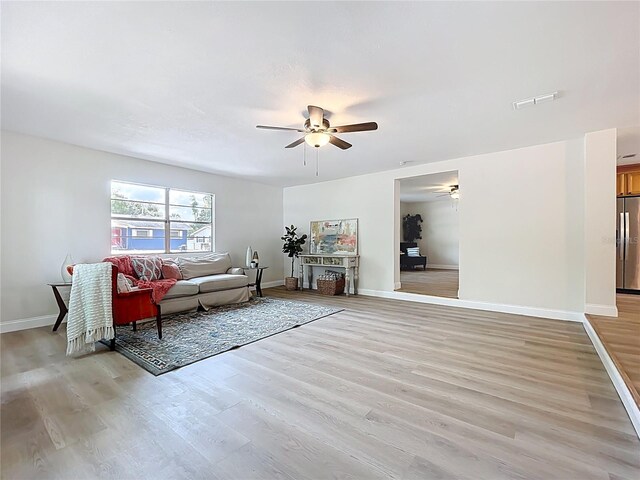 living room with a ceiling fan, light wood finished floors, and baseboards