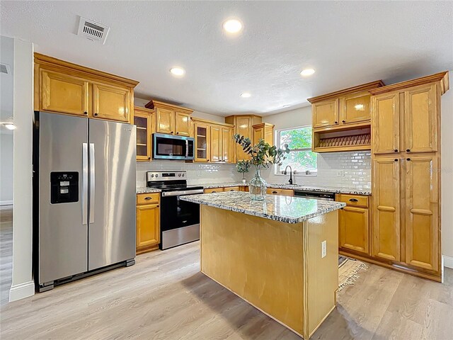 kitchen featuring stainless steel appliances, light wood-style floors, light stone counters, backsplash, and glass insert cabinets