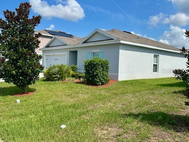 264 Fiddlewood Ct, Davenport, FL 33837 - view of side of home featuring an attached garage, stucco siding, and a yard