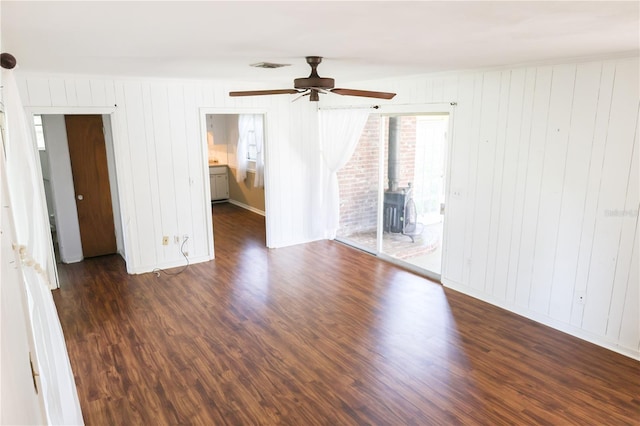 733 Oleander Dr SE, Winter Haven, FL 33880 - empty room with a wood stove, ceiling fan, dark wood-style floors, and wood walls
