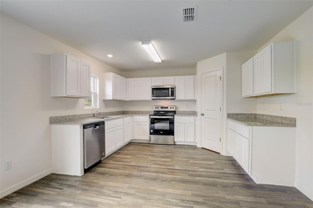 kitchen with sink, white cabinetry, light stone counters, appliances with stainless steel finishes, and light hardwood / wood-style floors