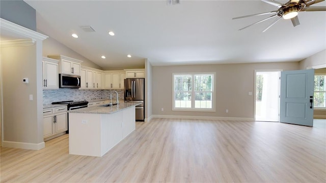 kitchen featuring stainless steel appliances, light stone countertops, ceiling fan, a center island with sink, and light hardwood / wood-style flooring