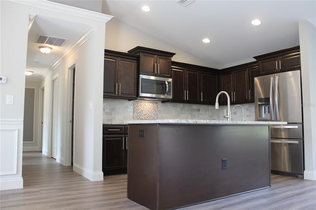 kitchen with backsplash, light stone countertops, light hardwood / wood-style flooring, and appliances with stainless steel finishes