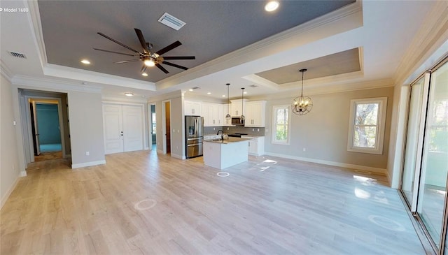 unfurnished living room featuring light hardwood / wood-style floors, a tray ceiling, ceiling fan with notable chandelier, and ornamental molding