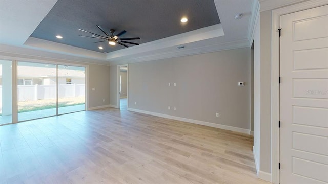 empty room with ornamental molding, ceiling fan, a tray ceiling, and light hardwood / wood-style flooring