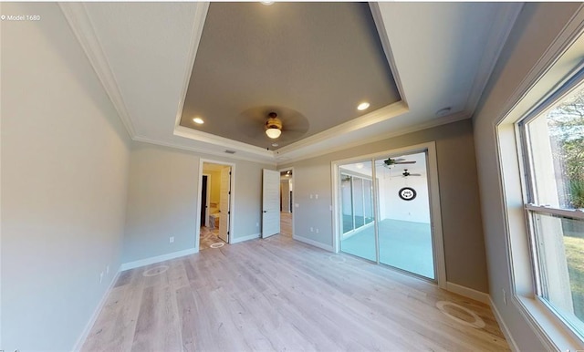 empty room with a raised ceiling, light hardwood / wood-style floors, ornamental molding, and ceiling fan