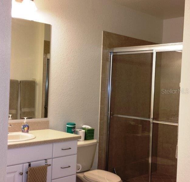 bathroom featuring toilet, a shower with door, and large vanity