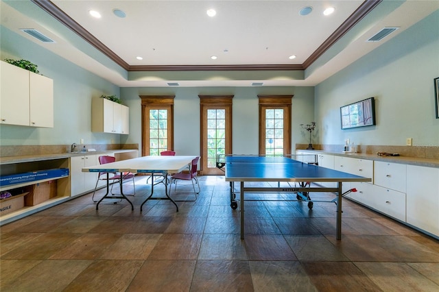 recreation room featuring dark tile floors, a tray ceiling, sink, and ornamental molding