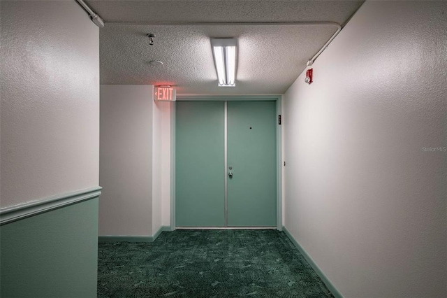 hallway featuring a textured ceiling and dark carpet