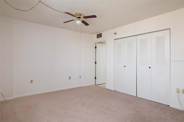 unfurnished bedroom featuring a closet, a textured ceiling, light colored carpet, and ceiling fan