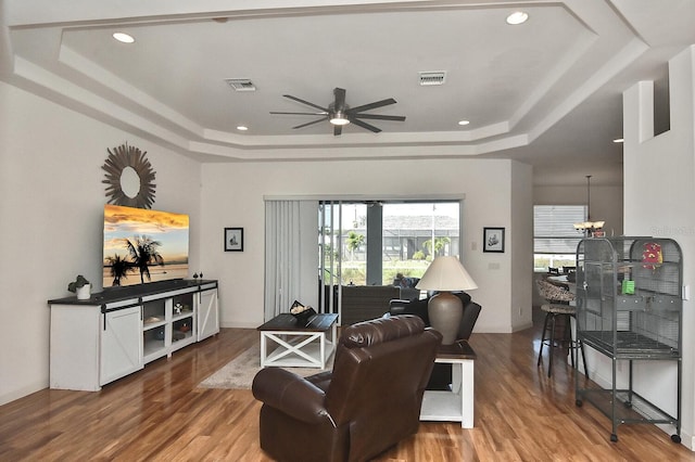 living room featuring ceiling fan with notable chandelier, a tray ceiling, and light wood-type flooring