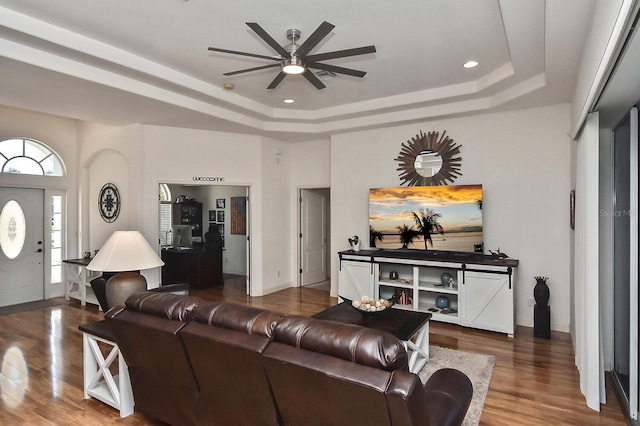 living room with a raised ceiling, hardwood / wood-style floors, and ceiling fan