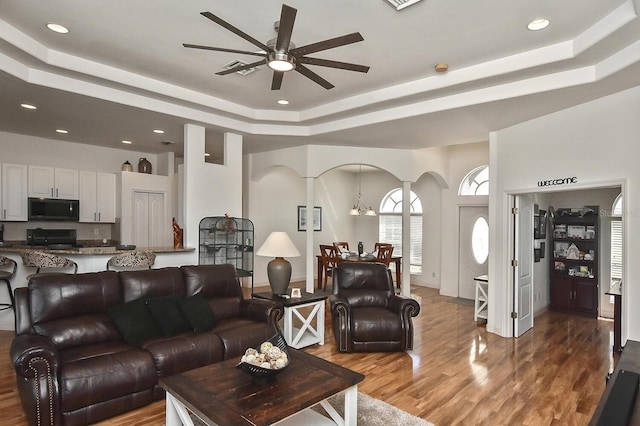 living room with a raised ceiling, hardwood / wood-style floors, and ceiling fan with notable chandelier