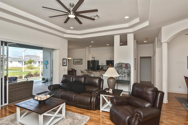 living room featuring ceiling fan, a tray ceiling, and light wood-type flooring