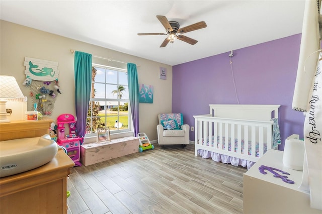 bedroom featuring light hardwood / wood-style flooring, ceiling fan, and a crib